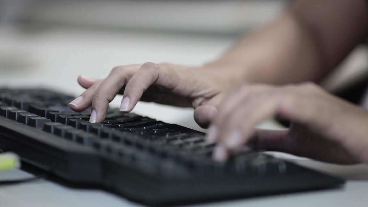 a imagem mostra duas mãos digitando em um teclado de computador preto